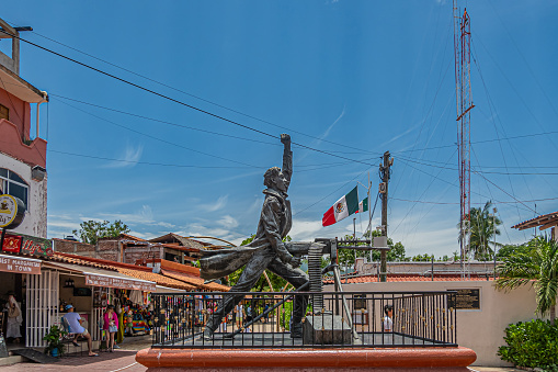Zihuatanejo, Mexico - July 18, 2023: Side view on Bronze Jose Azueta Abad statue in front of shopping street, Mexican Navy war hero during US occupation of Veracruz. Blue cloudscape