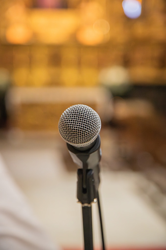 Microphone in the foreground ready to be used inside a church or religious space. Blurred church background.