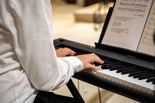 Detail of hands of a Caucasian man in classical clothing playing music on a keyboard in an interior church environment. Close up