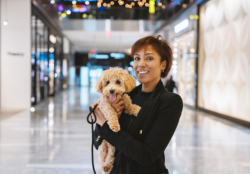 Mature woman posing with her toy poddle dog in a large shopping mall, New York City, USA