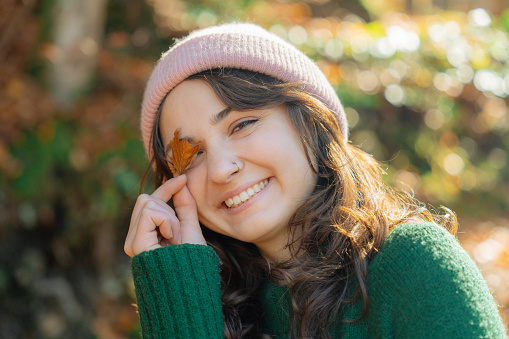 Portrait of cheerful  woman covering her eye with autumn leaf