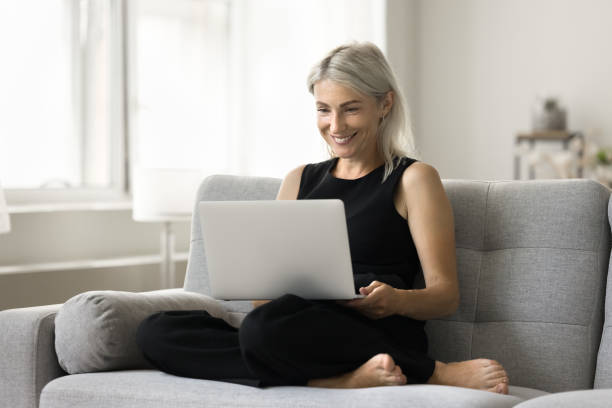 istock Happy mature freelancer woman sitting with gadget on home sofa 1708362726