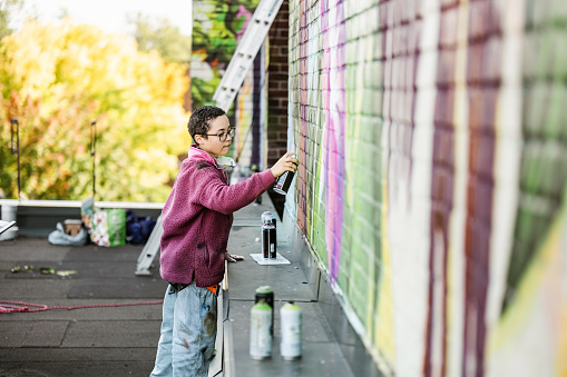 Young Mexican woman creating outdoor mural on the roof top wall. She is dressed in casual outfit. Exterior of old building in the city of Toronto, Canada..