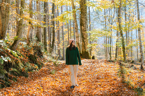 Cheerful woman in green sweater walking in forest in autumn