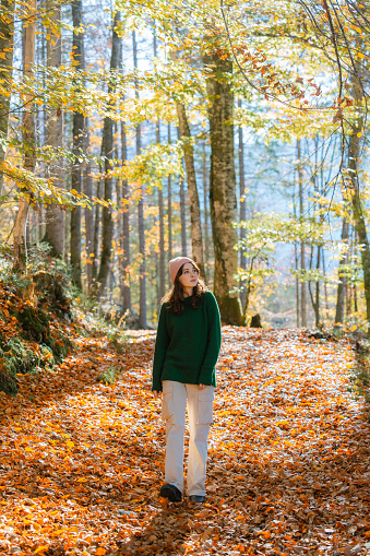 Cheerful woman in green sweater walking in forest in autumn