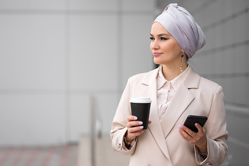Muslim woman enjoys spending free time during break surfing internet. Businesswoman in formal dress drinks coffee scrolling social media, close-up
