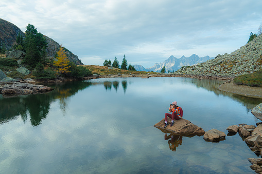 Woman in colourful sweater with camera  sitting  at the lake in Austria during the hike