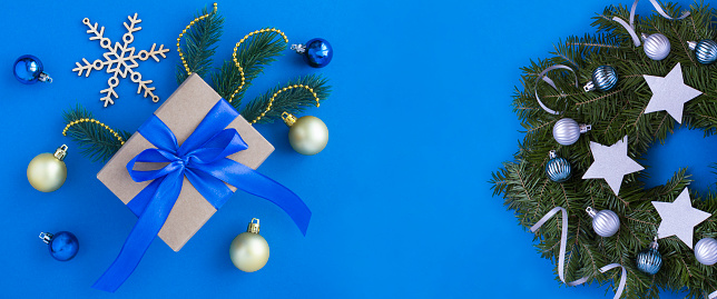 Christmas present with tied blue bow and Christmas ring or wreath on the blue background. Copy space. Top view.