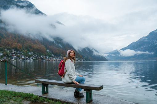 Woman with backpack  sitting on the bench and looking at Hallstattersee in autumn