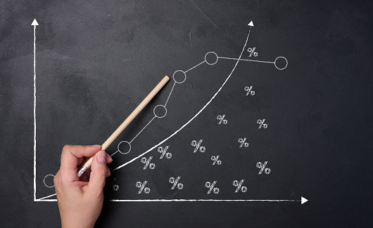 A woman's hand points to a graph with growing indicators drawn on a black chalkboard.