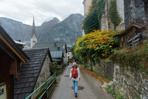 Cheerful woman in white sweater with backpack  walking in Hallstatt old town and exploring european culture