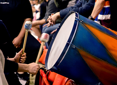 Football fan playing drums in the stands, close-up. He plays a blue and orange drum.