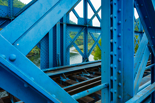 Section of an iron bridge painted blue with a train track over the Miño River in Orense, Spain