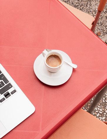 Espresso cup and laptop computer  on a red bar table.