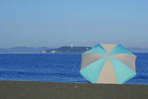 Enoshima and beach umbrellas.\nCoast of Chigasaki City, Kanagawa Prefecture, Japan.