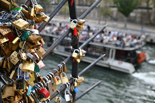 Paris, France-09 26 2023: Love locks attaches to a railing of a Paris bridge with a tour boat passing in the background, France.