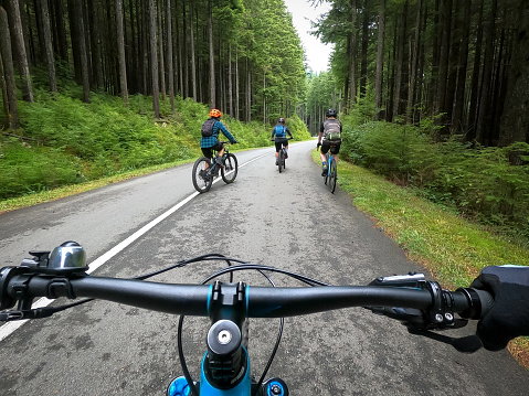 Group Ride - POV of diverse multi-generation, multiracial group of mountain bikers cycling on a forested autumn road.  North Vancouver, British Columbia, Canada.