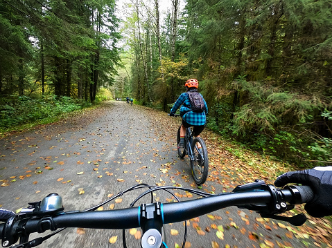 Group Ride - POV of diverse multi-generation, multiracial group of mountain bikers cycling on a forested autumn road.  North Vancouver, British Columbia, Canada.