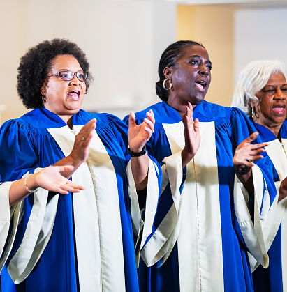 A group of three mature and senior women singing in a church choir wearing blue and white robes.