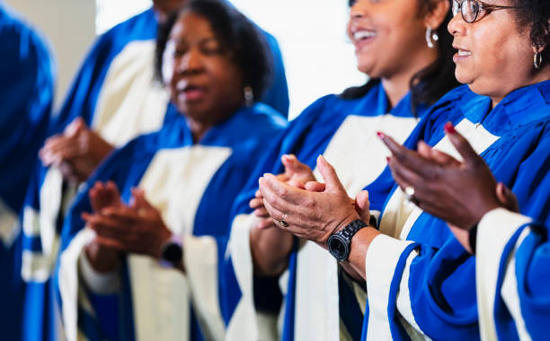 Cropped view of black men and women singing in choir Cropped view of a group of black and African-American men and women, mostly seniors, singing in a church choir, wearing blue and white robes. The focus the senior woman wearing eyeglasses. black gospel church stock pictures, royalty-free photos & images