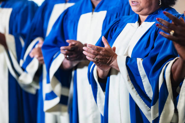 Cropped view of black men and women singing in choir Cropped view of a group of black and African-American men and women wearing blue and white robes singing together in a church choir. The focus is on the hands of one of the senior women. black female gospel singers stock pictures, royalty-free photos & images