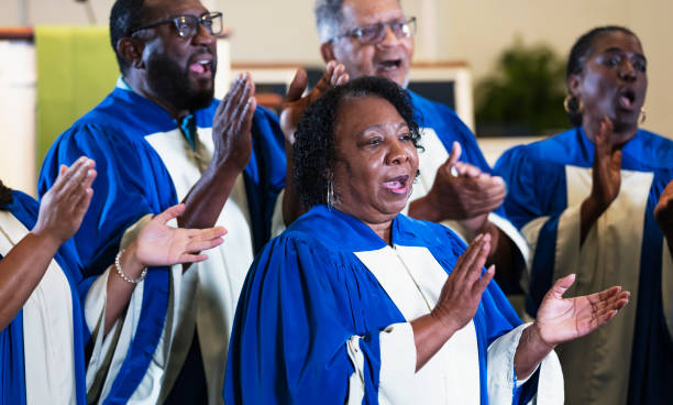 Senior black men and women singing in church choir A group of senior black and African-American men and women singing in a church choir, wearing blue and white robes. The focus is on the woman in the foreground. She is in her 60s. black female gospel singers stock pictures, royalty-free photos & images