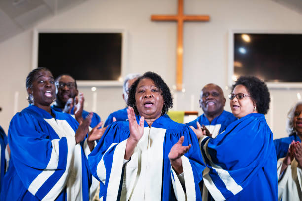 Senior African-American woman singing in church choir A group of mature and senior black and African-American men and women singing in a church choir, wearing blue and white robes. The focus is on the woman in the foreground who is in her 60s. black gospel church stock pictures, royalty-free photos & images