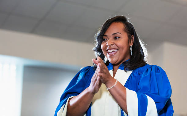 Mid adult black woman singing in church choir A mid adult African-American woman singing in a church. She is a member of the choir, wearing a white and blue robe. She is in her 30s. black gospel church stock pictures, royalty-free photos & images