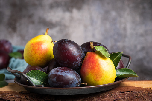 Fresh ripe plums and pears in a metal bowl on a gray-black background
