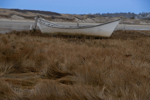 An abandoned white dory sits within the dunes of the beach in Northern New England with a stunning blue sky in the background.