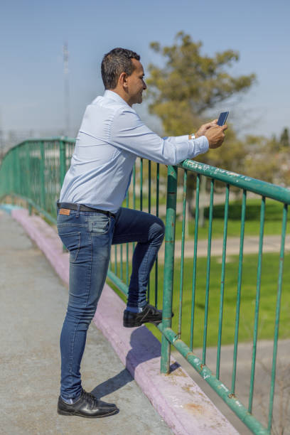 istock Latin man using his mobile phone leaning on the railing of a pedestrian bridge. 1708725632