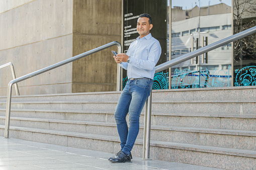 Latino man using a mobile phone on the stairs of a building.