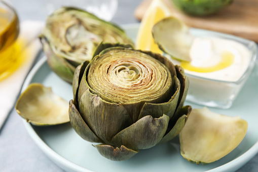 Delicious cooked artichokes with tasty sauce on plate, closeup