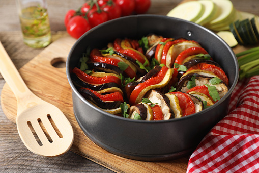 Delicious ratatouille in round baking pan and spatula on table