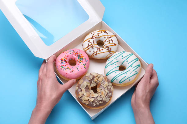 istock Woman taking tasty glazed donut from box on light blue background, top view 1708839029