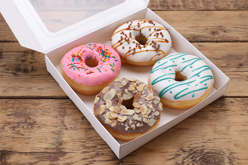 Box with different tasty glazed donuts on wooden table