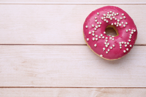 Tasty glazed donut decorated with sprinkles on white wooden table, top view. Space for text