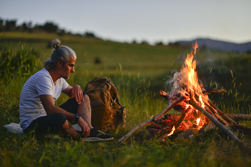 mountaineer traveling in nature, lighting a campfire, hiking, sitting and resting
