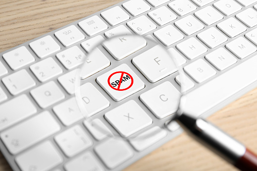 Prohibition sign with word Spam on keyboard button, view through magnifier