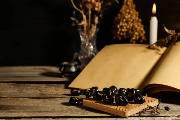 istock Composition with black rune stones and old book on wooden table. Space for text 1708886002