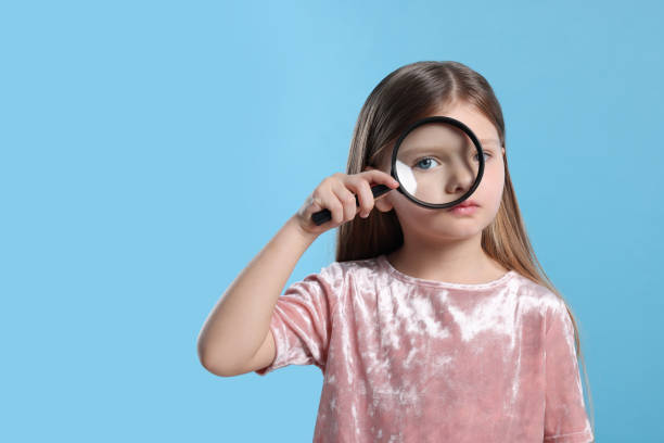 istock Cute little girl looking through magnifier glass on light blue background. Space for text 1708983932