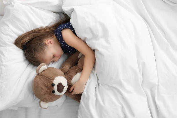 istock Cute little girl sleeping with teddy bear in bed, top view. Space for text 1708984457