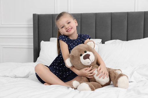 Cute little girl playing with teddy bear on bed