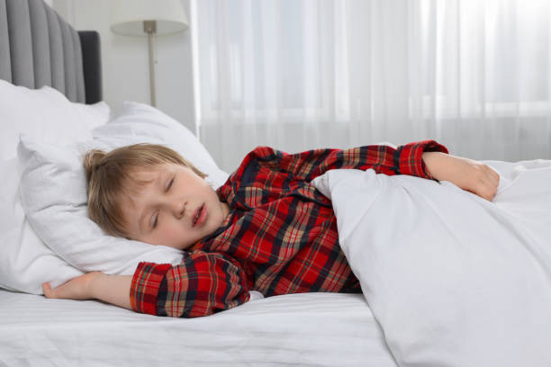 A young boy with a pensive expression rests his head on an orange sofa, looking relaxed and contemplative indoors.