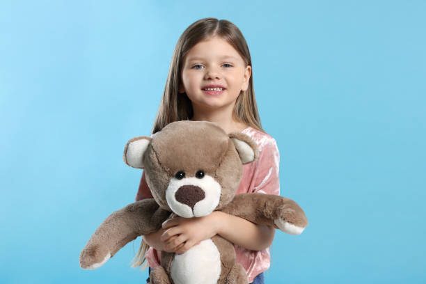 istock Cute little girl with teddy bear on light blue background 1708986638
