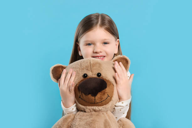 istock Cute little girl with teddy bear on light blue background 1708987170