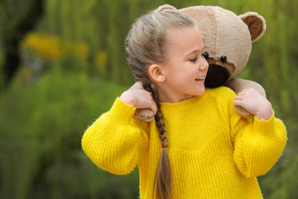 Cute little girl with teddy bear outdoors. Space for text