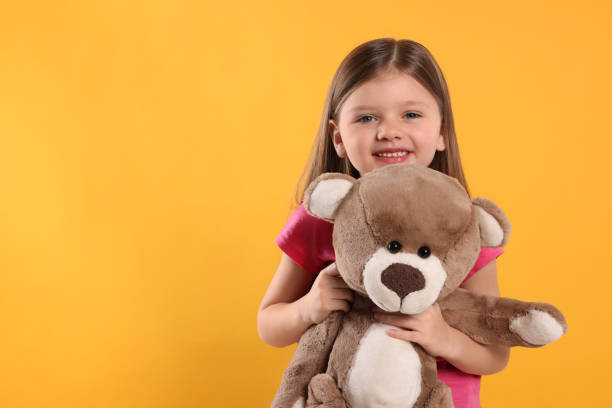 istock Cute little girl with teddy bear on yellow background. Space for text 1708987193