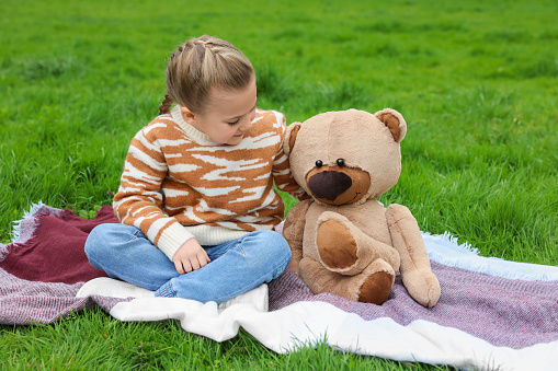 Little girl with teddy bear on plaid outdoors