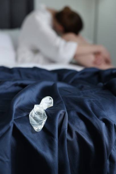 frau, die auf dem bett sitzt und das kondom im schlafzimmer ausgerollt hat, selektiver fokus. safer sex - sexually transmitted disease bed women worried stock-fotos und bilder